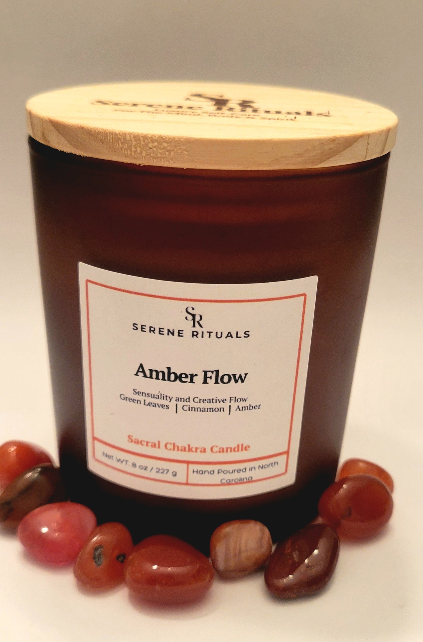 Serenity Rituals Amber Flow candle with wooden lid and surrounding Carnelian stones on a neutral background