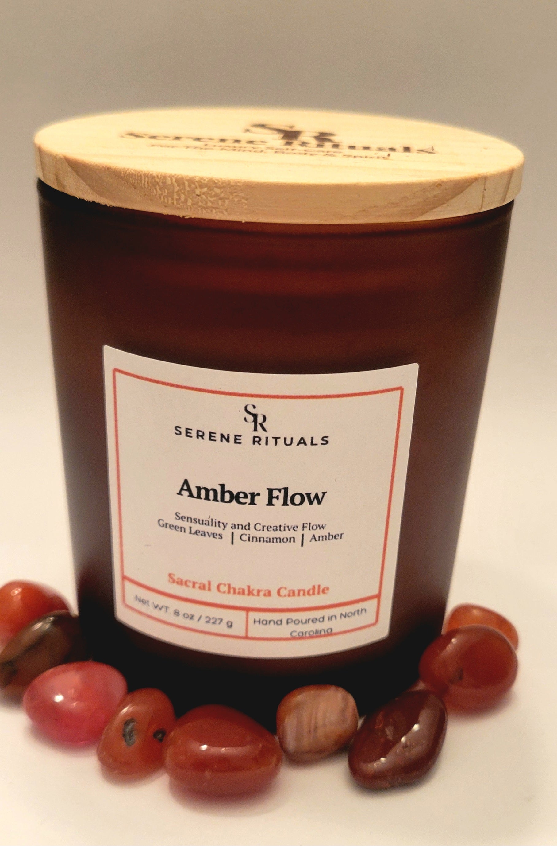 Serenity Rituals Amber Flow candle with wooden lid and surrounding Carnelian stones on a neutral background