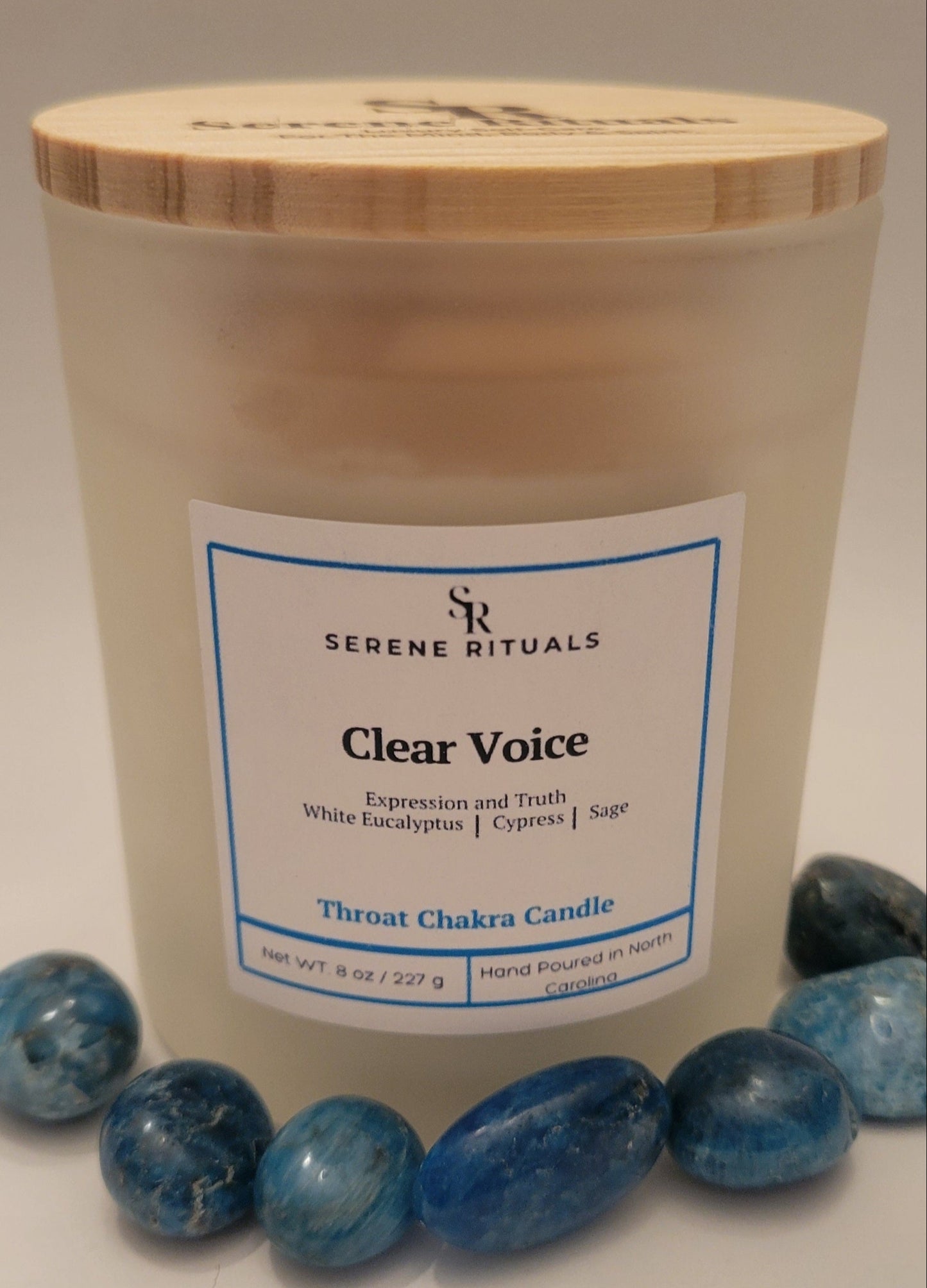 Clear Voice Throat Chakra candle by Serene Rituals with a wooden lid and blue stones on a light background