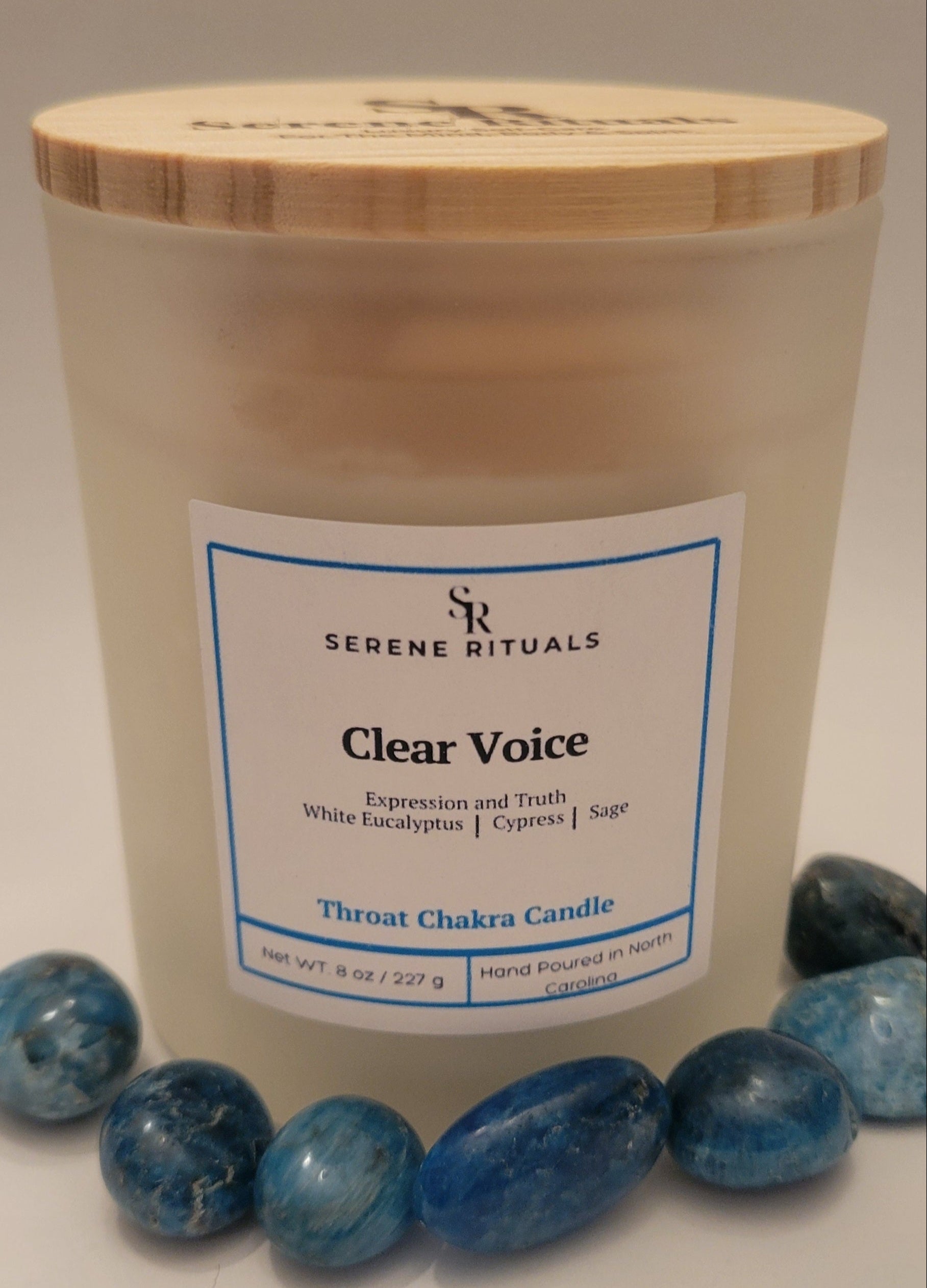 Clear Voice Throat Chakra candle by Serene Rituals with a wooden lid and blue stones on a light background
