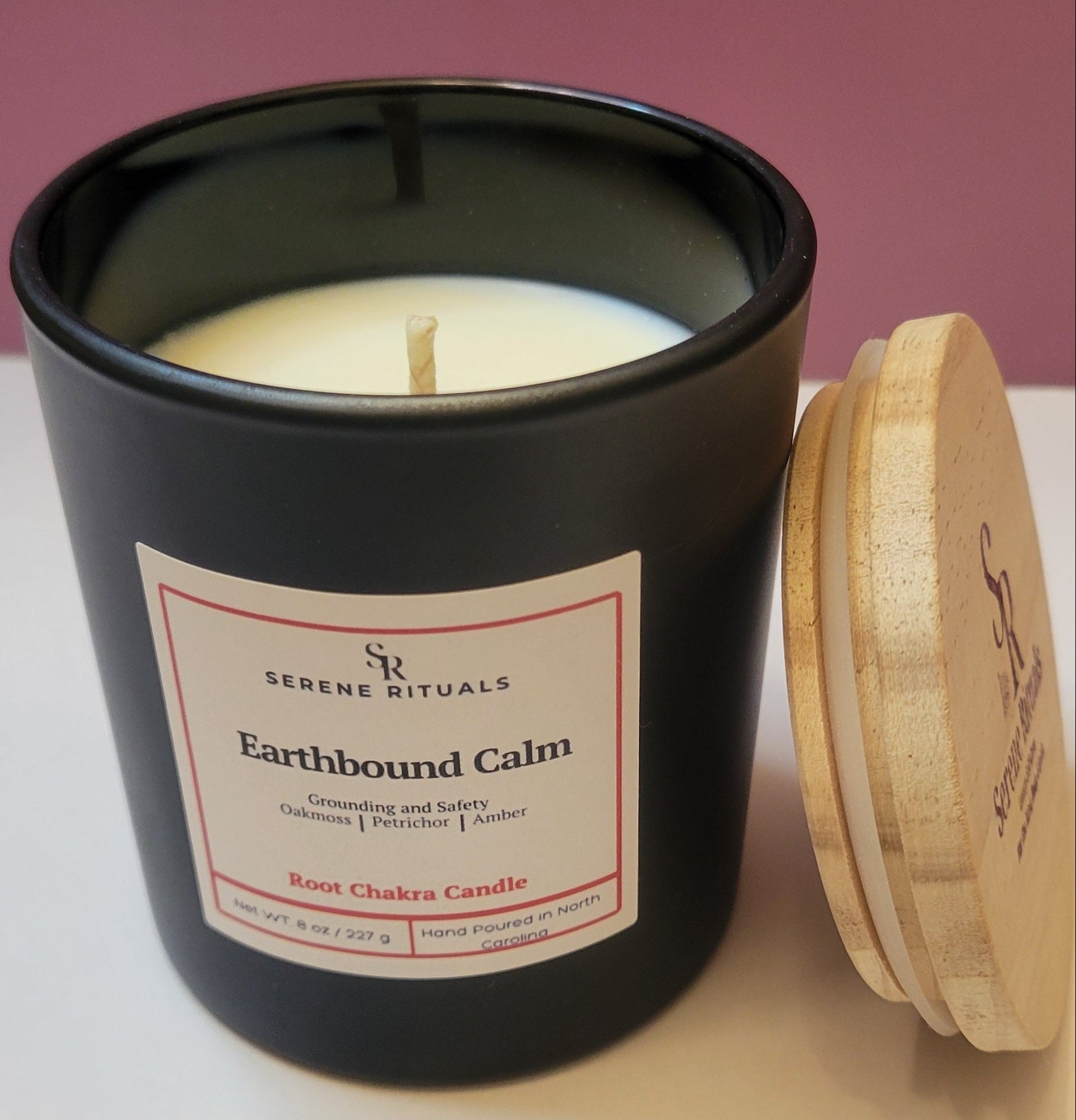 Earthbound Calm scented candle in a black container with a wooden lid on a white surface.