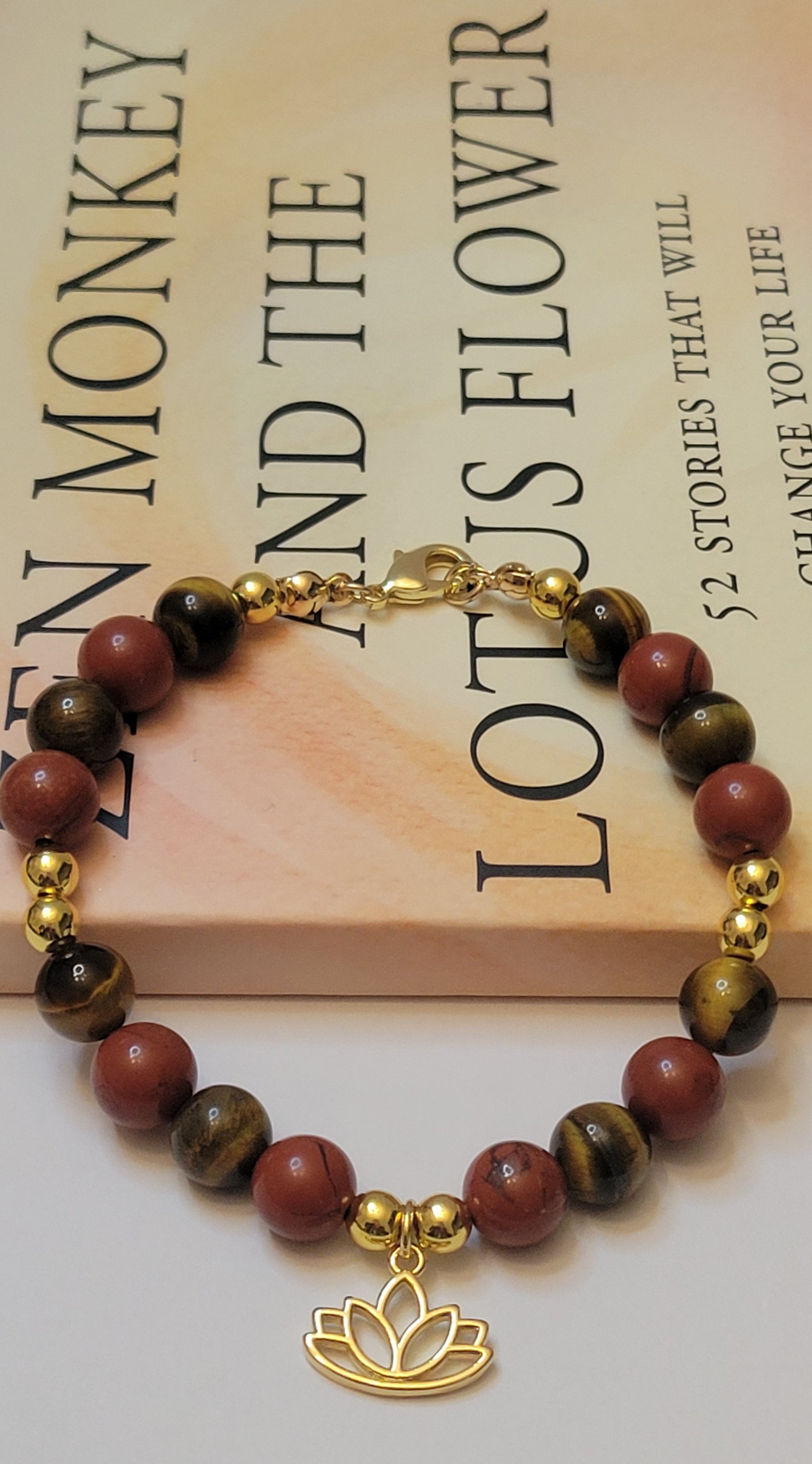 Fearless Strength Bracelet with Tiger's Eye and Red  Jasper beads and gold lotus charm on a book background