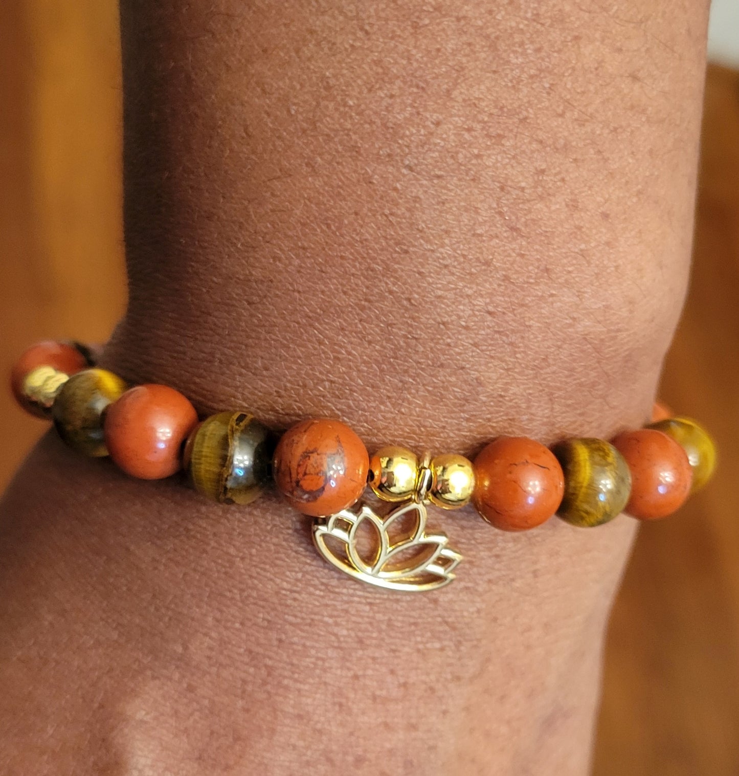Fearless Strength Bracelet with Tiger's Eye and Red  Jasper beaded design with a gold lotus charm on a wrist against a neutral background