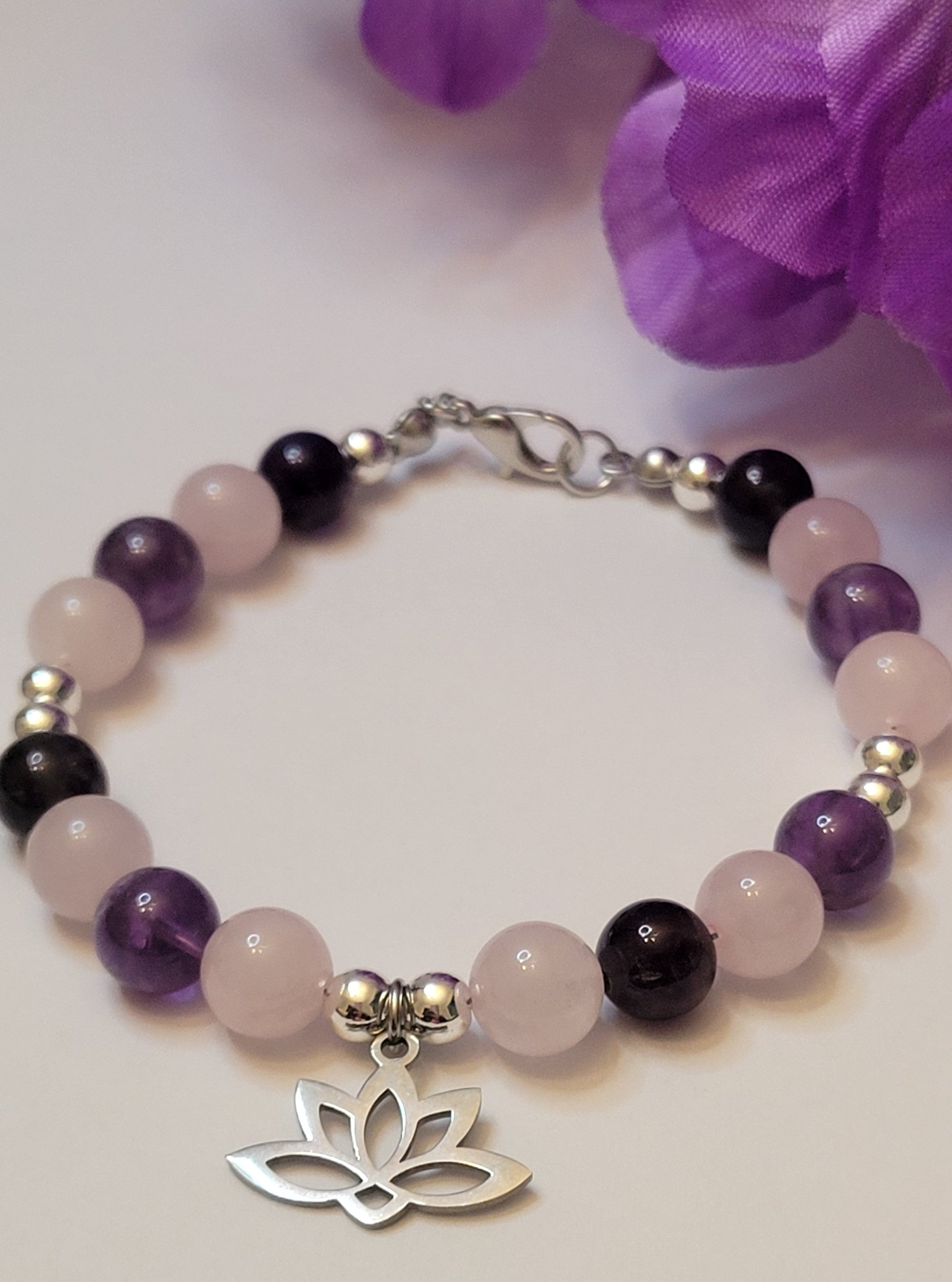 Heart and Soul Bracelet with Amethyst and Rose Quartz beads and lotus charm on a white background with purple flowers.