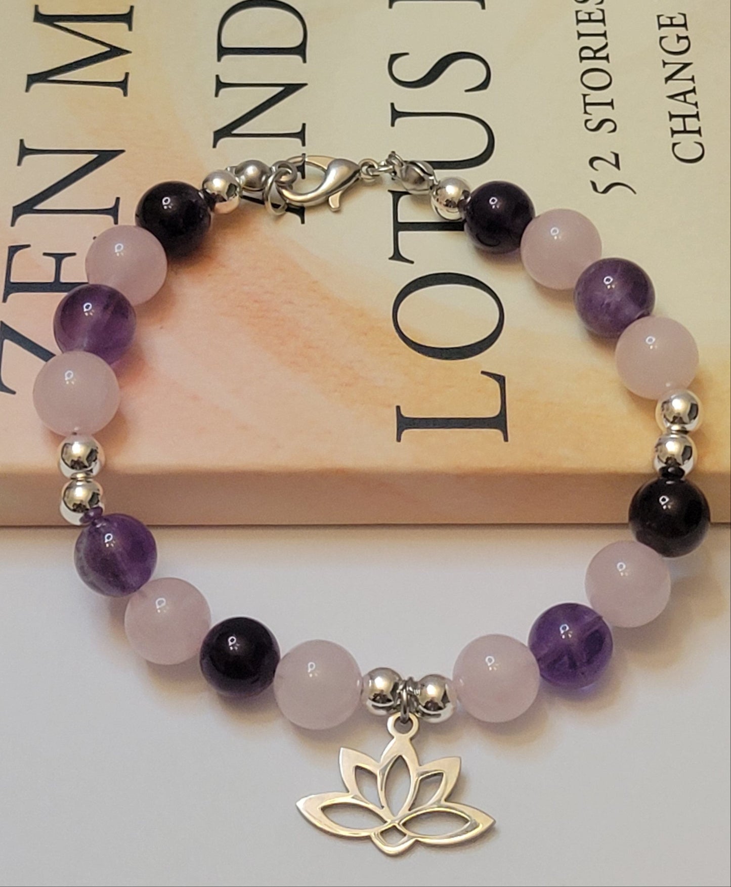 Heart and Soul Bracelet with Amethyst and Rose Quartz beads and a lotus flower charm on a book background