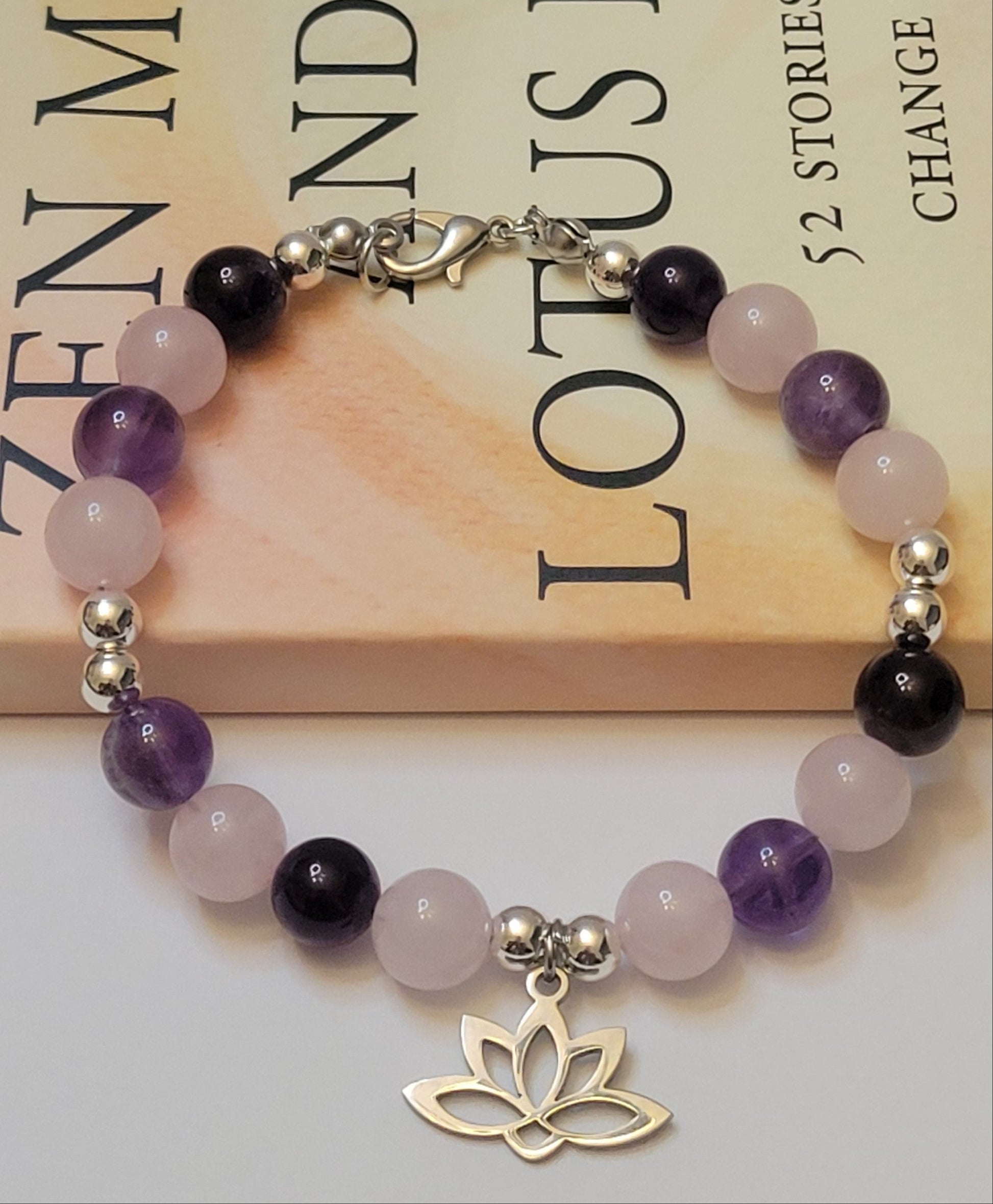 Heart and Soul Bracelet with Amethyst and Rose Quartz beads and a lotus flower charm on a book background