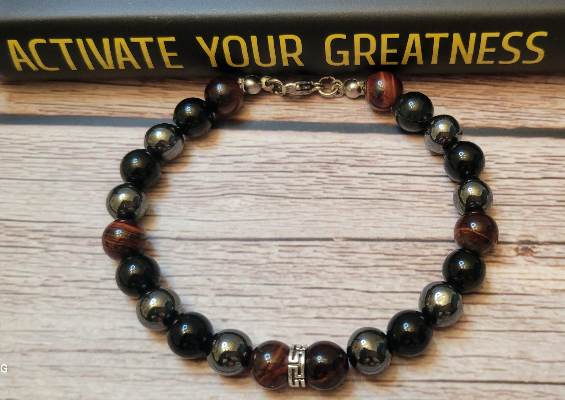 Midnight Armor gemstone  bracelet with black Obsidian, Red Tiger's Eye, and Hematite gemstone beads on a wooden surface with 'Activate Your Greatness' book in the background.