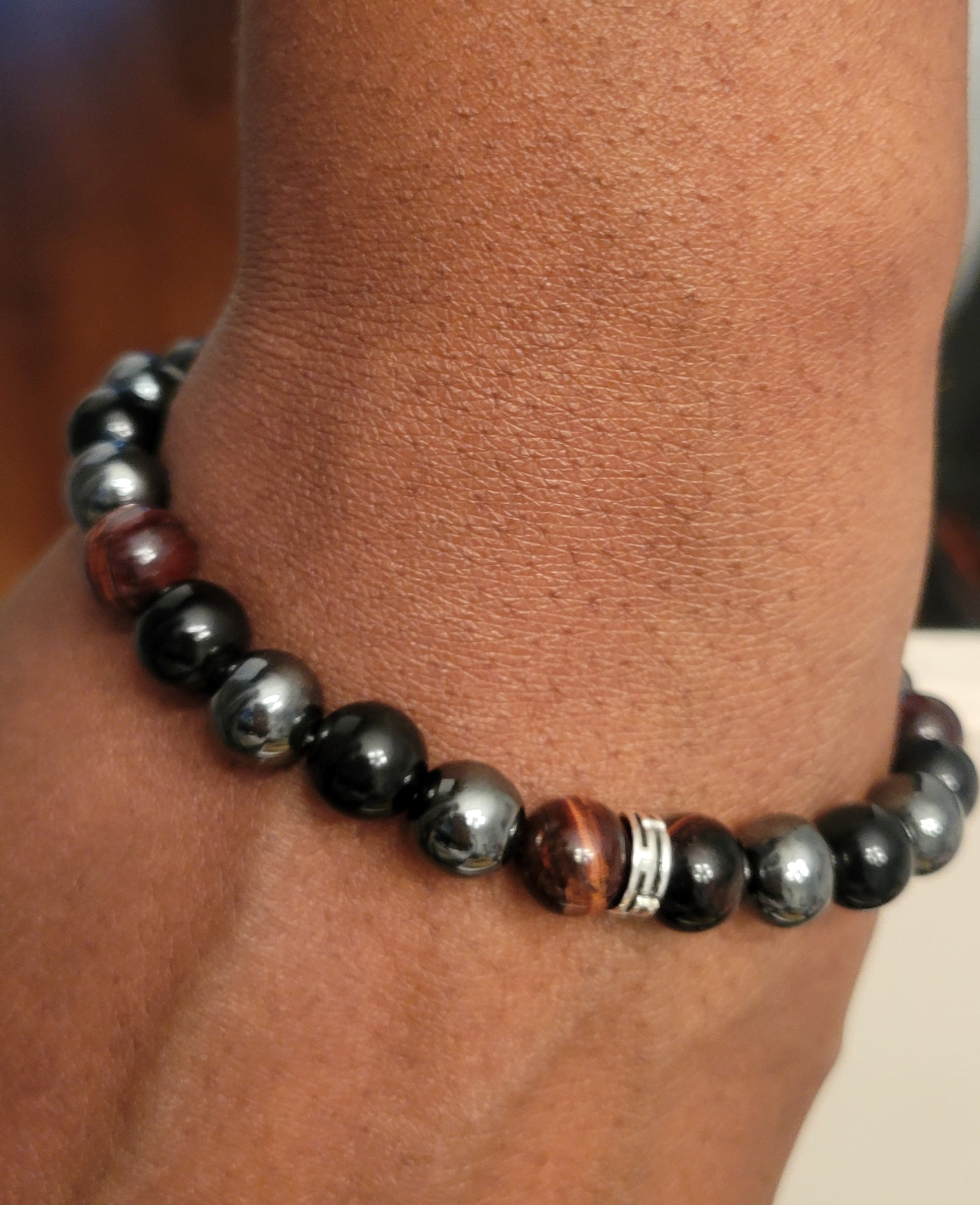 Close-up of a person's wrist wearing a Midnight Armor bracelet with black Obsidian, Red Tiger's Eye, and Hematite gemstone beads.