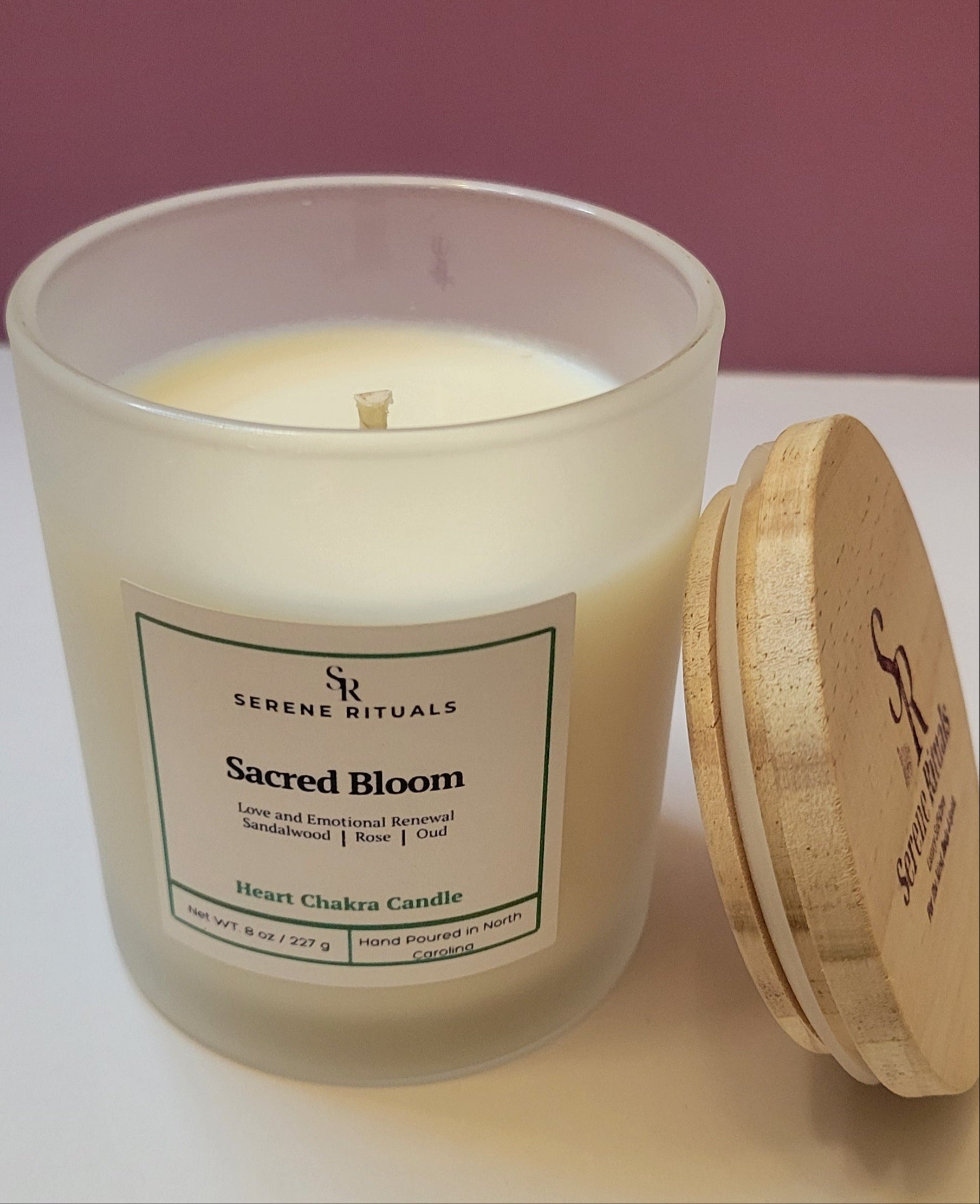 Candle in a glass jar with a wooden lid on a white surface, against a pink background