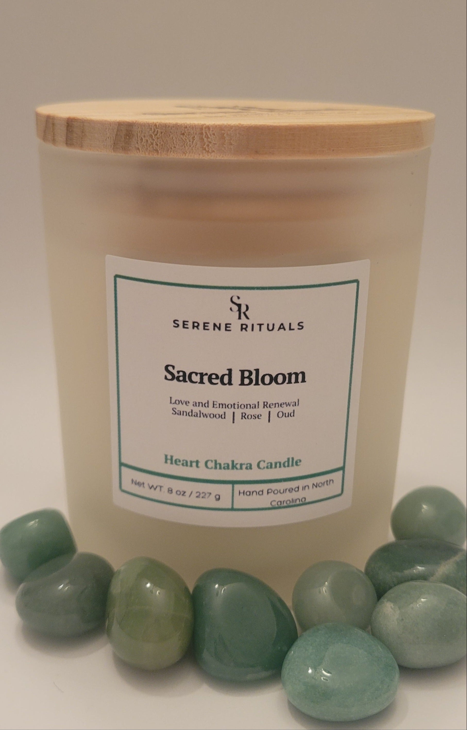 Candle labeled 'Sacred Bloom' from Serene Rituals with Green Aventurine stones on a neutral background