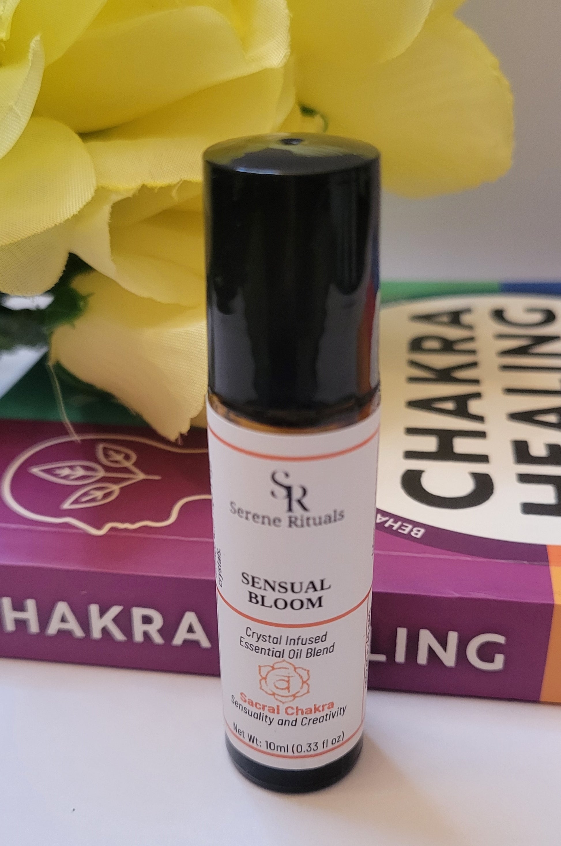 Serene Rituals Sensual Bloom essential oil blend bottle with yellow flowers and 'Chakra Healing' book in the background.