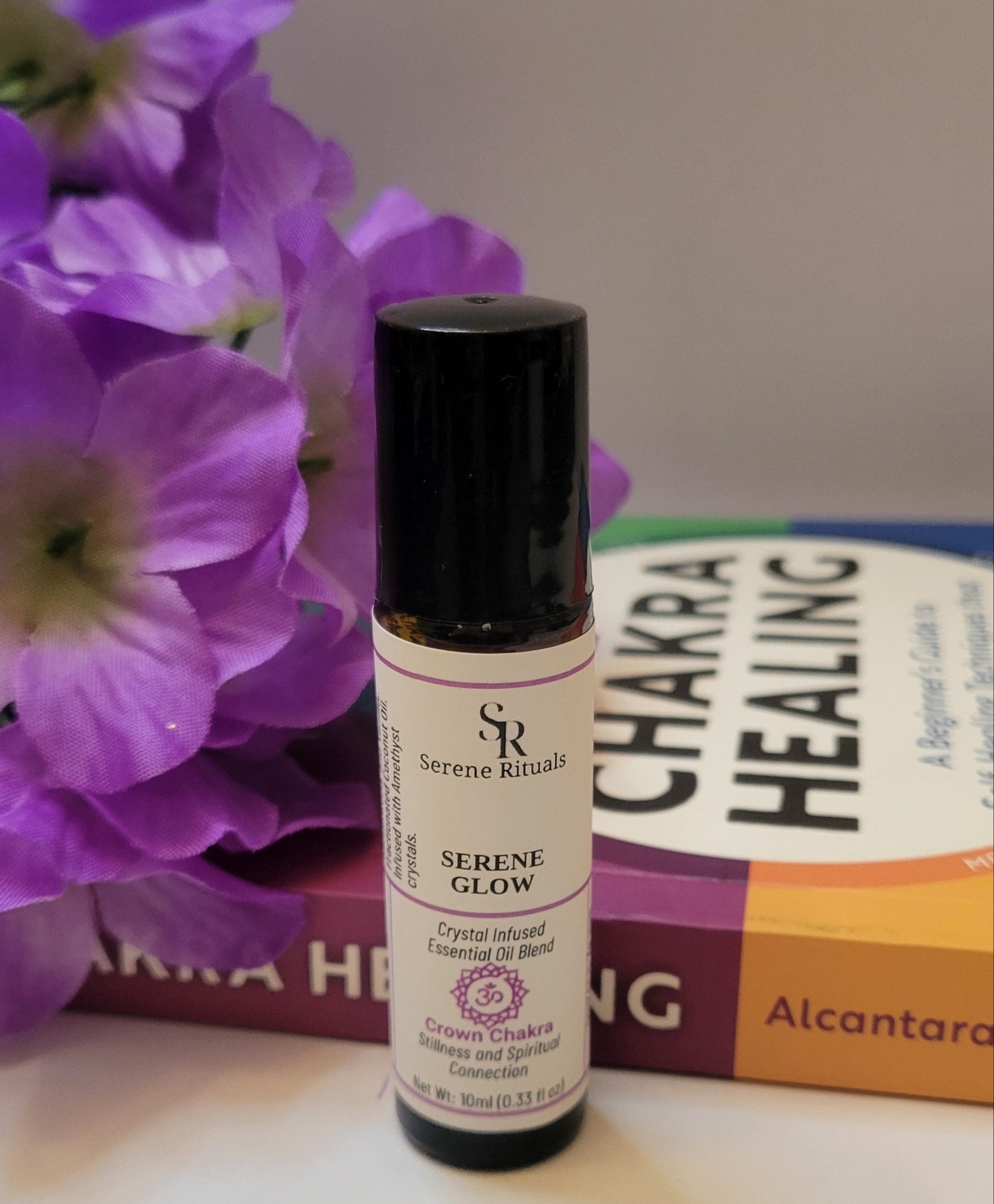 Serene Glow essential oil bottle with purple flowers and a book in the background.