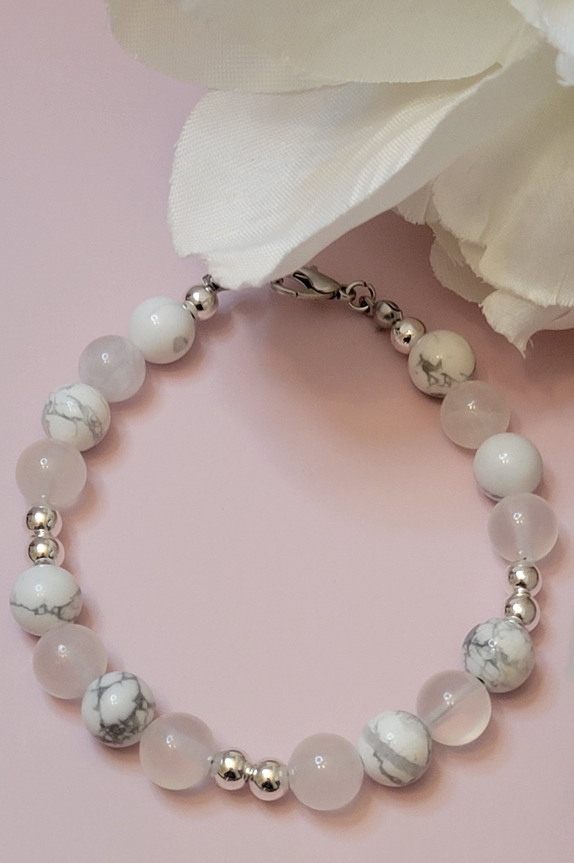 Serenity Glow Bracelet with Howlite and Selenite  beads  and silver accents on a pink background with a white flower.